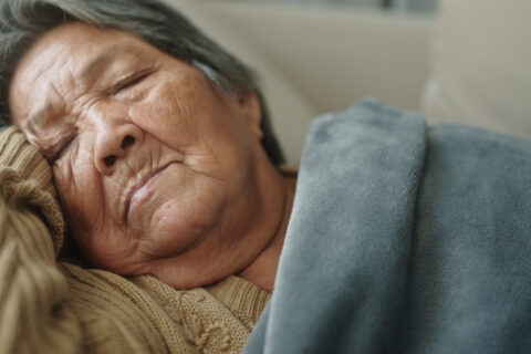 A hospice patient lies on a couch with a blanket someone brought to her in her Portland, OR home