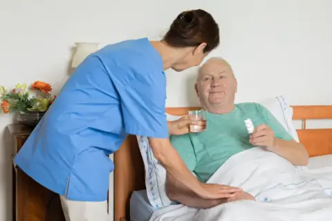 A hospice worker gives medication and water to a patient