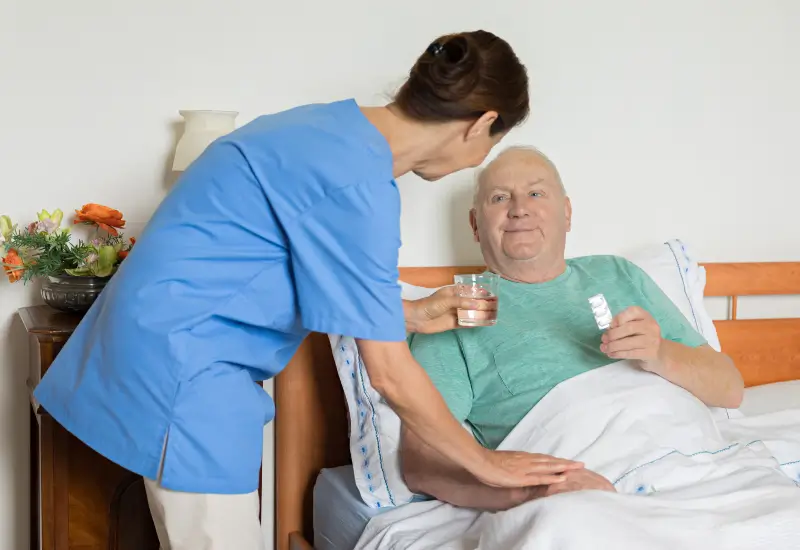 A hospice worker gives medication and water to a patient