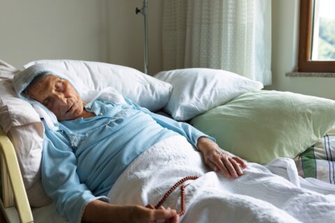 A woman in hospice care at home holds prayer beads near the end of her life