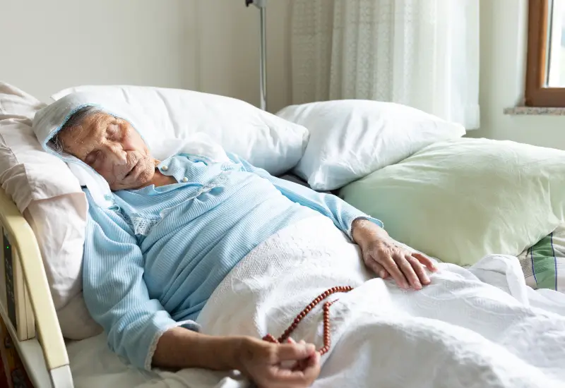 A woman in hospice care at home holds prayer beads near the end of her life