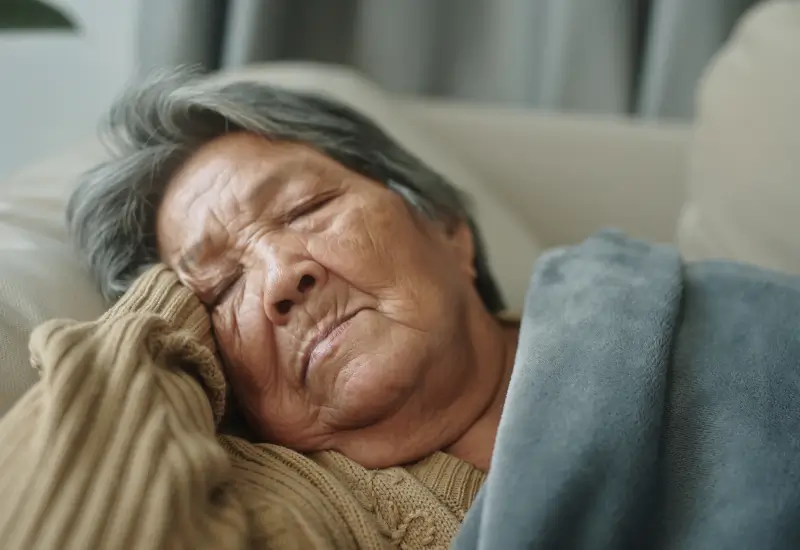 A hospice patient lies on a couch with a blanket someone brought to her in her Portland, OR home