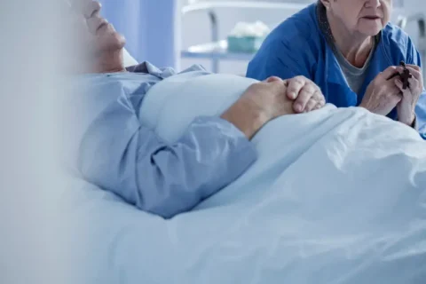 A woman prays at a man’s bedside in hospice care in Portland, OR