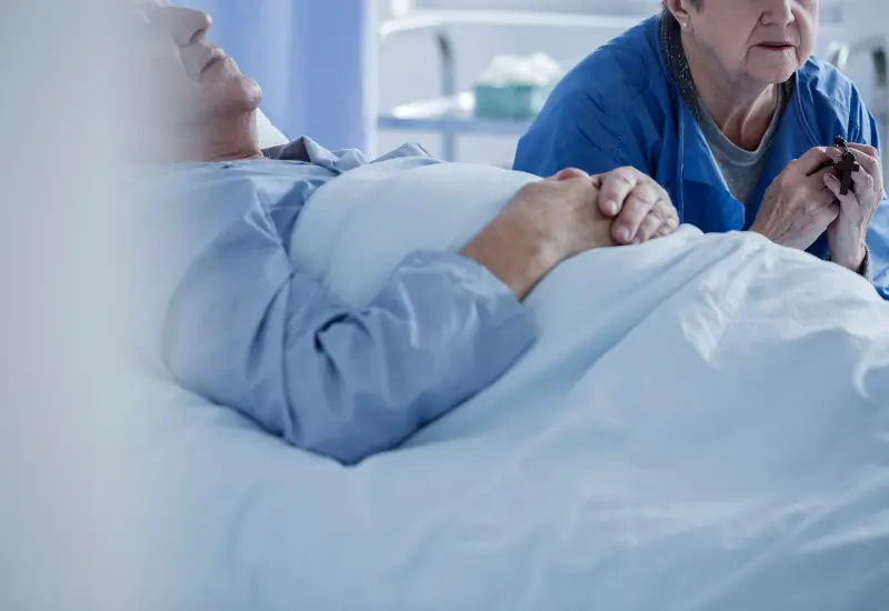 A woman prays at a man’s bedside in hospice care in Portland, OR