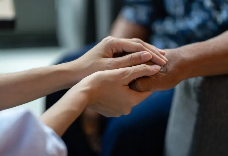 An in-home hospice care worker holds hands with a patient in Portland, OR